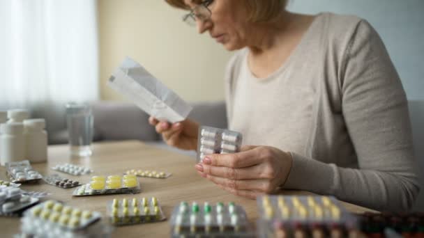 Malata vecchia seduta a casa a tavola e a leggere pillole istruzione, medicina — Video Stock