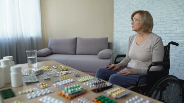 Депрессивная старуха, сидящая в инвалидной коляске возле стола с лекарствами, одиночество — стоковое видео