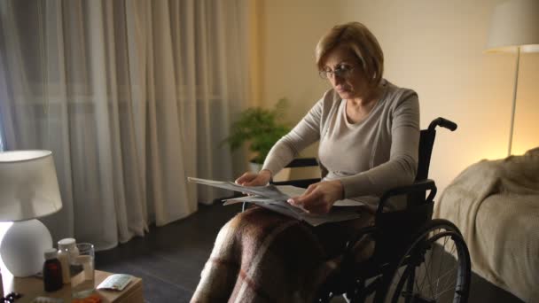 Vieja sentada en silla de ruedas y leyendo periódicos en casa, problema de salud — Vídeo de stock