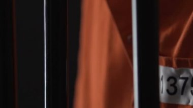 Kızgın mahkum turuncu tulum cep barlar, seri katil eller closeup holding