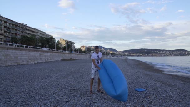 Mladý muž, nafouknutí a vleže na pohovce putyka vychutnat odpočinek na pláži moře — Stock video