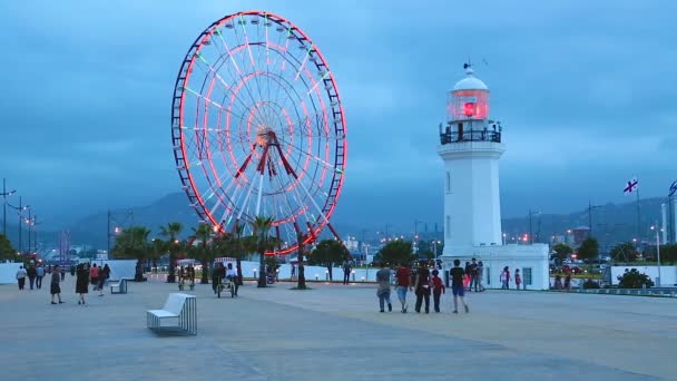 Mensen wandelen door enorme reuzenrad en licht huis in Batumi, Georgië — Stockvideo