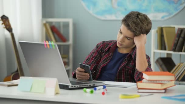 Uttråkad kille rullning appar på telefonen, distraherad från läxor, förhalning — Stockvideo