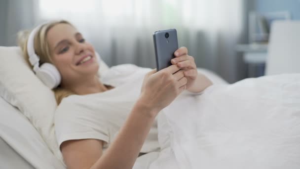 Reggel az ágyban, tinédzser lány fejhallgató viselése és a hálózati kommunikáció — Stock videók
