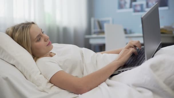 Adolescente sonriente que se comunica en las redes sociales, acostado en la cama, por la mañana — Vídeos de Stock