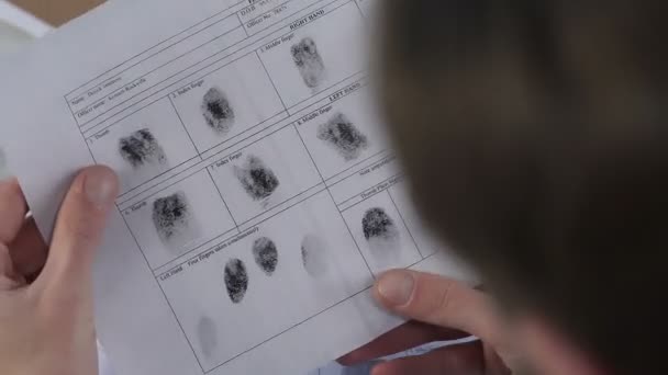 Офицер полиции проверяет файл с отпечатками пальцев с увеличительным стеклом, идентифицирует — стоковое видео