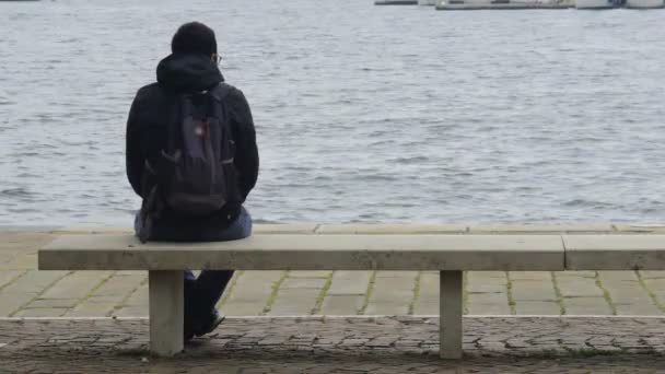 思いやりのある若い男はベンチに座って、海を見て背面、レクリエーション — ストック動画