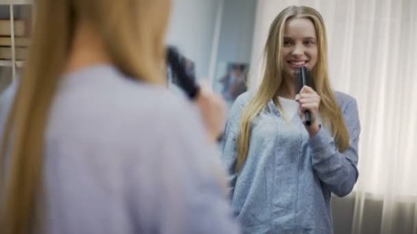 Attraktive junge Dame singt zur Haarbürste und träumt am Mikrofon von einer Star-Karriere — Stockvideo