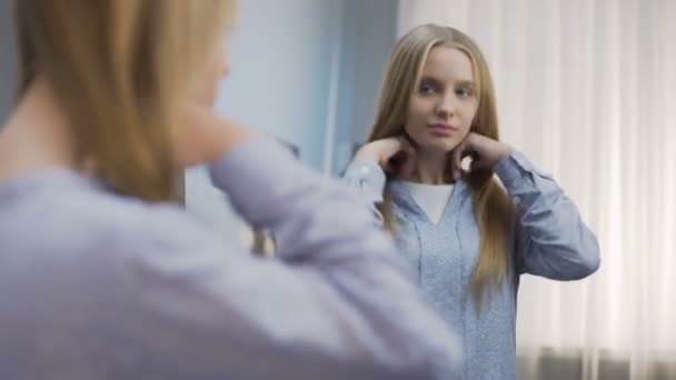 Bonita chica de la escuela tratando de diferentes peinados en el espejo, preparándose para la fiesta — Vídeo de stock