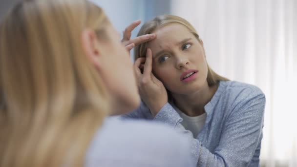 Занепокоєна молода жінка стискає прищі на обличчі перед дзеркалом, невпевненість — стокове відео