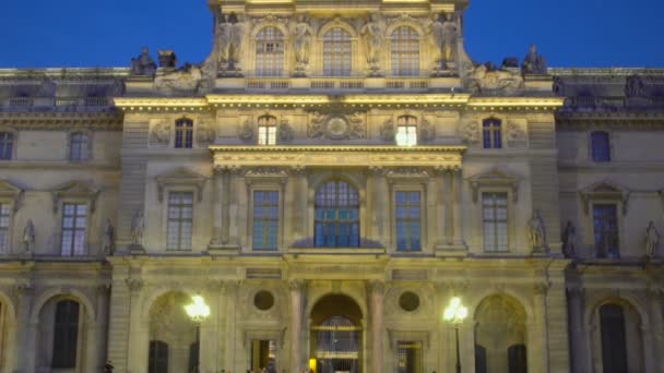 Paris, Frankrijk - Circa januari 2016: Sightseeing in de stad. Gevel van het Louvre paleis verlicht met lantaarns, toeristische menigte lopen, uitzoomen — Stockvideo