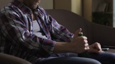 Kanepede oturan ve çatalla, umutsuzluk bira şişesini açmaya çalışırken tek adam