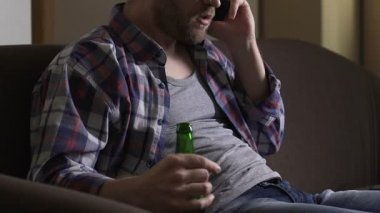 Kızgın bağımlısı adam kanepede oturan, telefonda konuşmak ve bira içmek