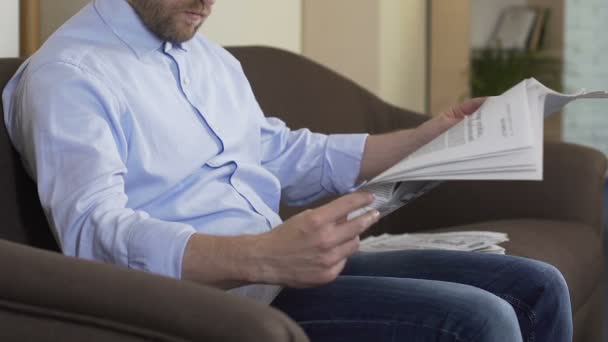 Дорослий чоловік сидить на дивані і читає газету додому, поточні події, дозвілля — стокове відео