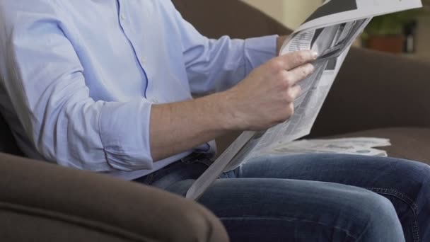 Чоловік в окулярах читає газету і посміхається, ранковий ритуал, вільний час — стокове відео