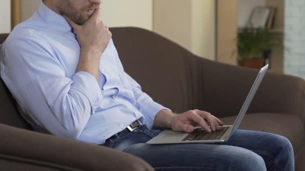 Успішний фрілансер чоловічої статі сидить на домашньому дивані і працює на ноутбуці, Інтернеті — стокове відео