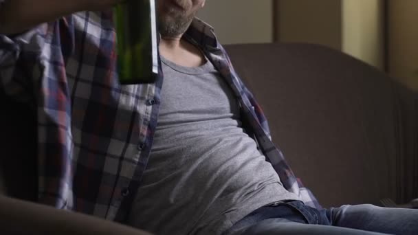 Unemployed man in his 30s sitting on couch and drinking bottled beer, depression — Stock Video