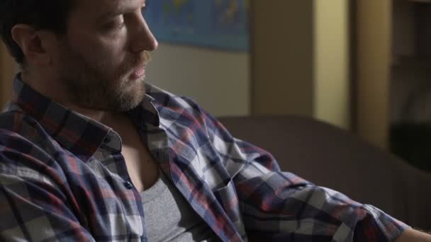 Ayyaş erkek kanepede oturan ve evde, bira şişesiyle alkolizm konuşuyor — Stok video