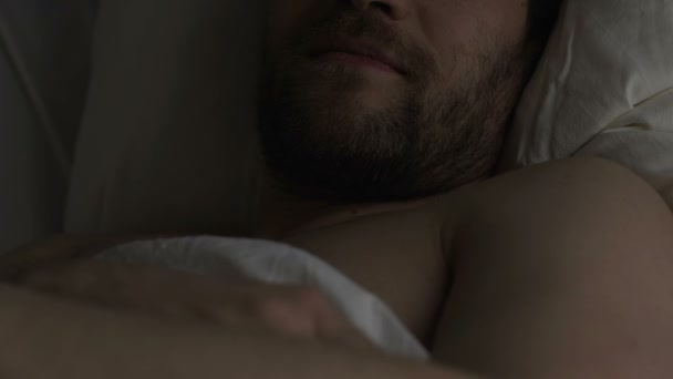 Здоровий задоволений чоловік лежить в ліжку, думаючи про свою дівчину і посміхаючись — стокове відео