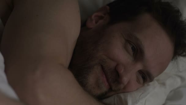 Homem adulto deitado na cama, sorrindo antes de adormecer, pensando no último encontro — Vídeo de Stock
