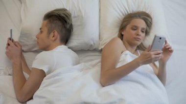Genç adam ve kadın akıllı telefonlar yatakta, gadget bağımlılığı arkaya yazmaya