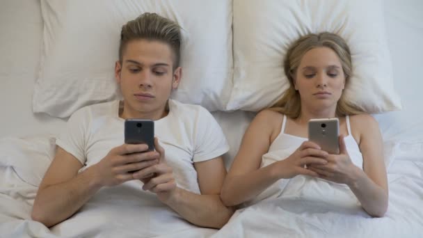 Jovem casal deitado na cama com smartphones, vício gadget afetando as relações — Vídeo de Stock