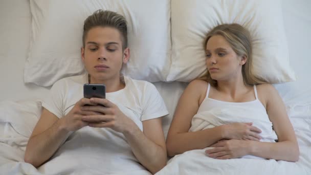 Angry girl looking at boyfriend using cellphone in bed, internet addiction — Stock Video