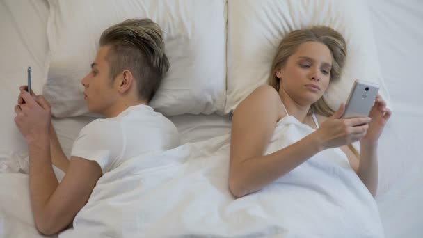 Молодая пара серфинг интернет на мобильном телефоне в постели лежа спина к спине, равнодушие — стоковое видео