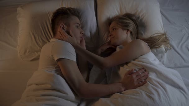 Feliz pareja joven acostada en la cama por la noche y cogidas de la mano, relaciones fuertes — Vídeos de Stock