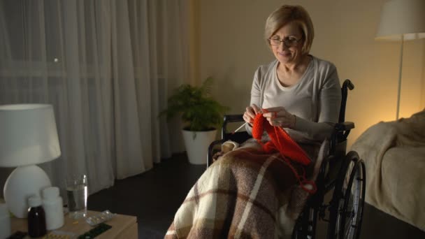fröhliche alte Frau sitzt im Rollstuhl und strickt Schal, kümmert sich um Kinder