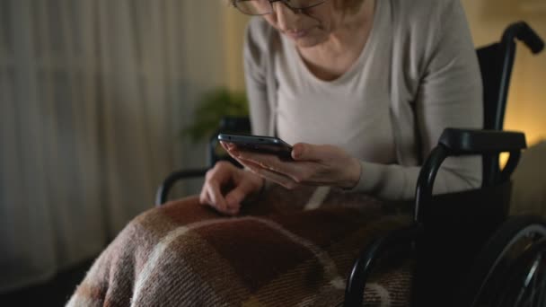 Старуха в инвалидном кресле просматривает фотографии на смартфоне, любит внуков — стоковое видео