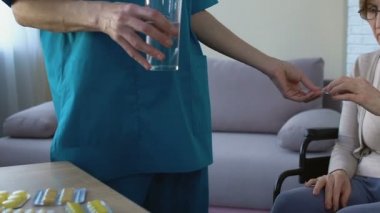 Hapları vermeye kadın hemşire yaşlı kadın destekleyen kadında tekerlekli sandalye, üzgün