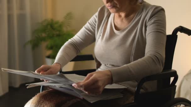 Mujer inteligente en silla de ruedas leyendo periódico, ocio de la vejez, tiempo libre — Vídeo de stock