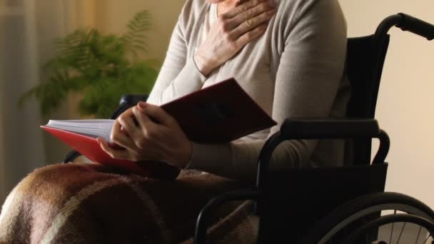 Frau im Rollstuhl betrachtet Fotoalbum und erinnert sich an glückliche Jugendmomente — Stockvideo