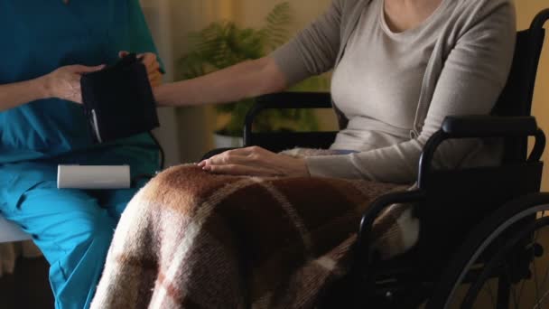 Bereitschaftsarzt misst Blutdruck, gehorsamer Patient sitzt im Rollstuhl — Stockvideo