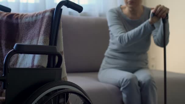 Грустная старшая леди смотрит на инвалидное кресло, чувствует себя одиноким и покинутым, депрессия — стоковое видео