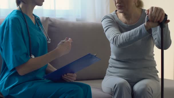 Fürsorgliche Krankenschwester fragt ältere Frau nach ihrer Gesundheit und füllt Krankenversicherung aus — Stockvideo