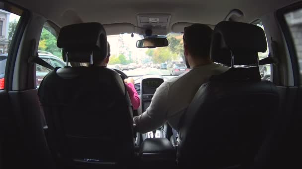 Husband helping his wife drive properly, holding steering wheel, city traffic — Stock Video