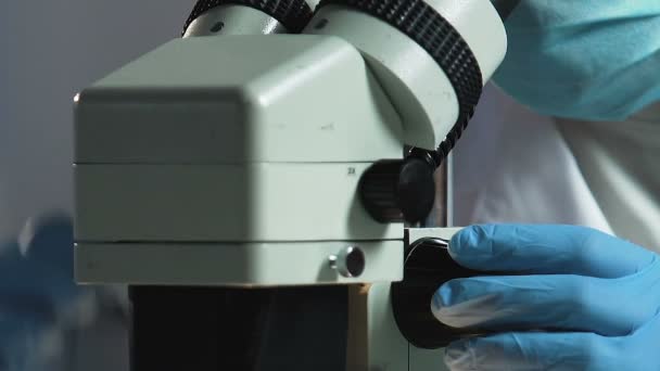 Adli bilim adamı dikkatle mikroskop closeup altında fiziksel delil inceliyor — Stok video