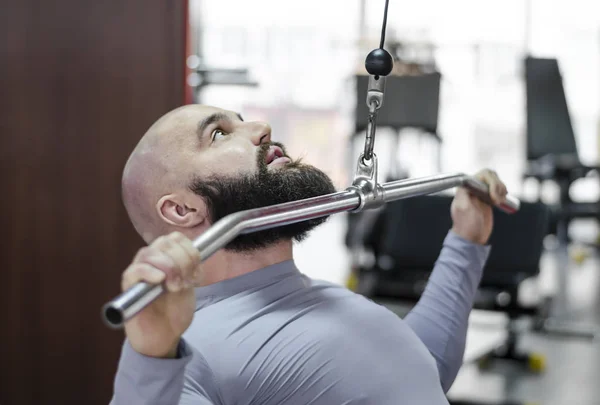 Мужчина спортсмен делает упражнения на пулдаун-машине в тренажерном зале, здоровый образ жизни — стоковое фото