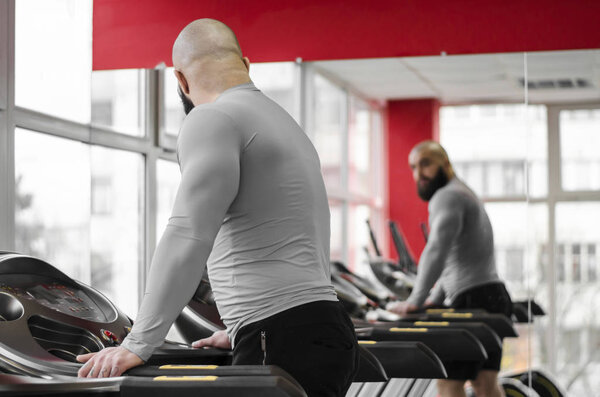 Man training on treadmill, looking at his reflection in mirror after workout