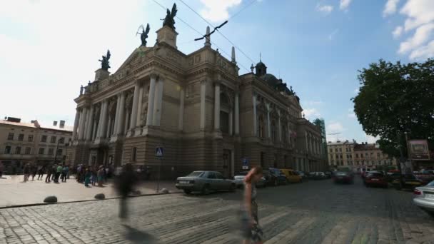 LVIV, UCRANIA - CIRCA JULIO 2017: Personas en la ciudad. Los peatones cruzan la carretera cerca de hermoso edificio histórico en el día soleado, Lviv — Vídeo de stock