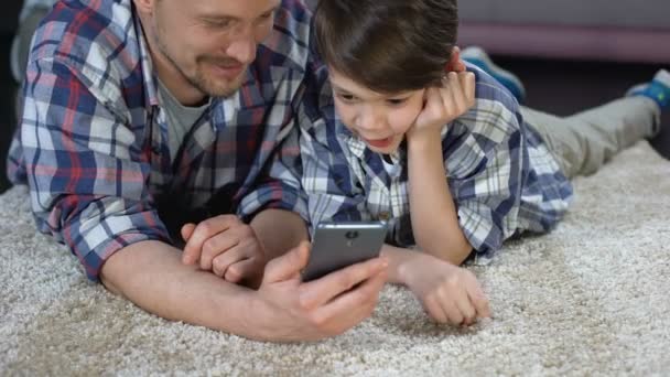 Niño y padre jugando juegos de teléfonos inteligentes en el suelo, esperando a mamá del trabajo — Vídeo de stock