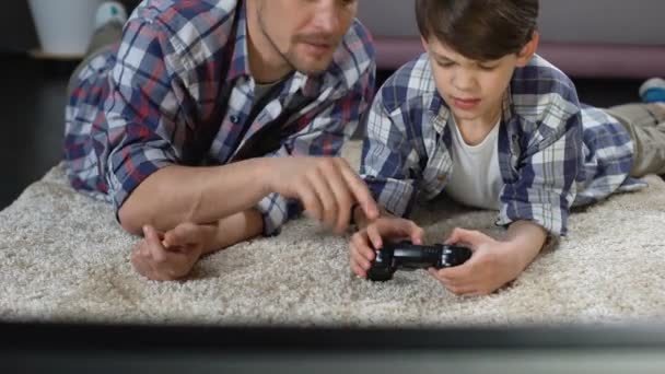 Papà cercando di aiutare il figlio a operare con il joystick del videogioco, il supporto e la cura — Video Stock