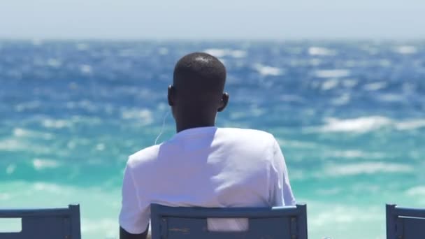 Νίκαια, Γαλλία - Circa Ιουνίου 2016: Οι άνθρωποι στην παραλία. Αφρικανική άνθρωπος στα ακουστικά να ακούτε μουσική στο seaside, απολαμβάνοντας θέα φύση — Αρχείο Βίντεο