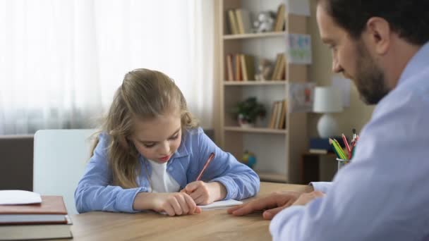 Sonriente Hija Pequeña Sentada Mesa Haciendo Tarea Con Padre Cuidado — Vídeo de stock