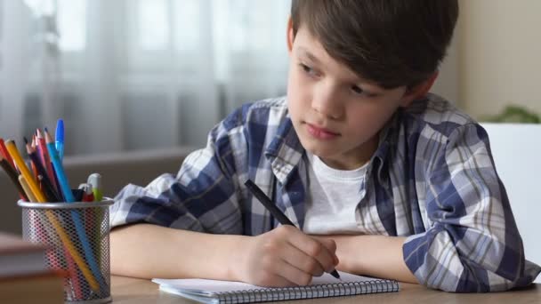 Скучный школьник делает домашнюю работу, смотрит в окно с сожалением, крупным планом — стоковое видео