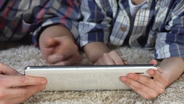 Son and father playing tablet game lying on home floor, family togetherness — Stock Video