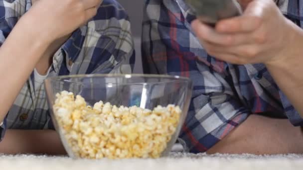 Сын и отец смотрят кино и едят поп-кукурузу из стеклянной чаши, свободное время — стоковое видео