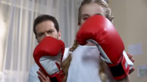 Chica de la escuela en guantes de boxeo puñetazos y mostrando sí gesto con el padre detrás — Vídeos de Stock